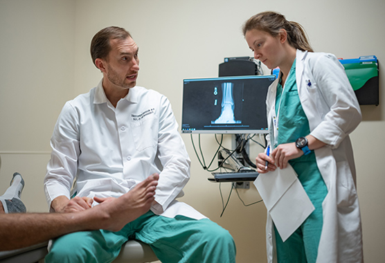 Two providers examining a patient’s foot for joint disorders in a clinic room.