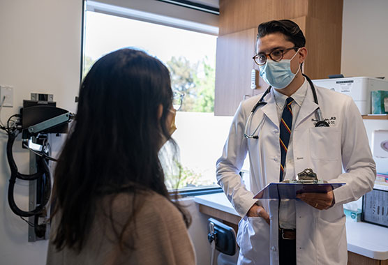 Male health care provider talking to female patient, both wearing masks