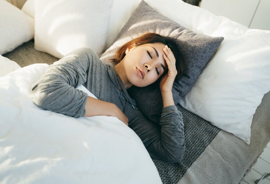 Woman lying in bed with her eyes closed and her hand on her head