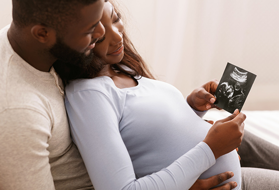 Man and pregnant woman hugging looking at an ultrasound of their child.