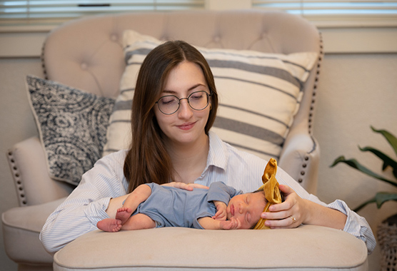 Mother sitting on the ground looking lovingly at her baby sleeping.