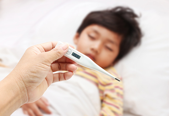 Sick boy in bed with measles as parent takes temperature with a thermometer.