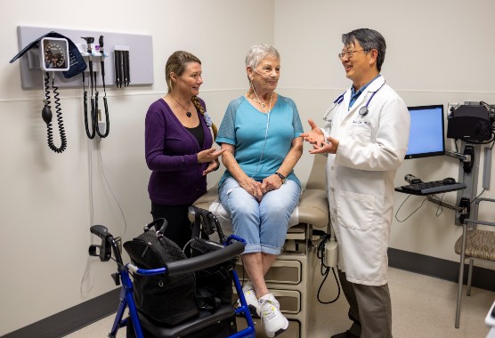 Older woman sitting on an exam table with younger woman and male physician next to her