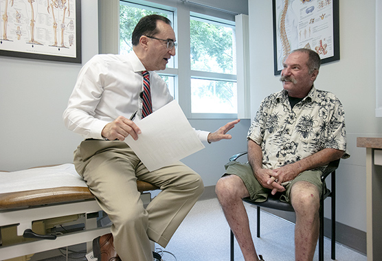 Male health care provider talking to older male patient in a clinic room.