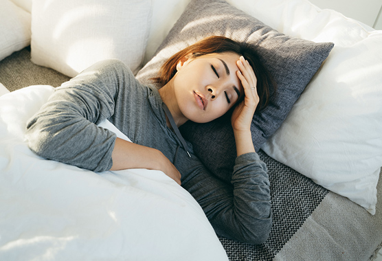 Young woman with hand on forehead lying in bed and feeling sick.