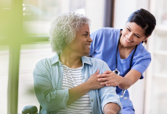 A mature woman looking back and smiling at a female nurse who holds her hand