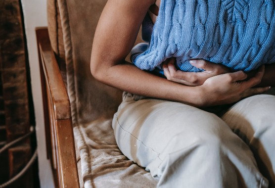 Close-up of a woman on a couch hunched over with her hand on her lower stomach in pain