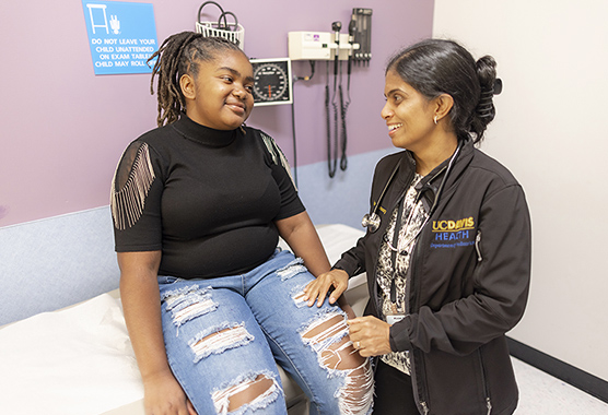 Young girl sitting on an exam table with female health care provider talking to her.