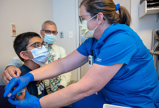 A pediatric patient getting a shot from a female provider while a male physician comforts him 