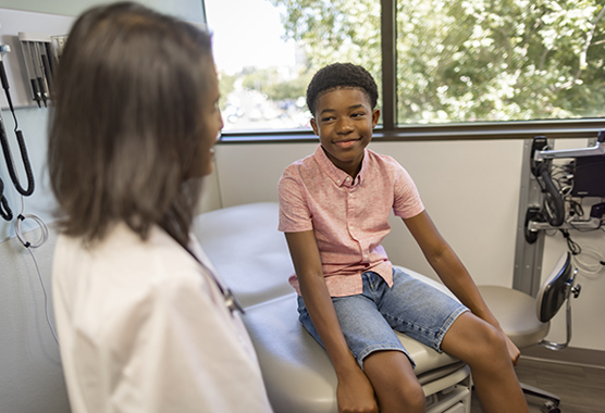Young boy sitting on an exam table smiling at his pediatric neurologist.