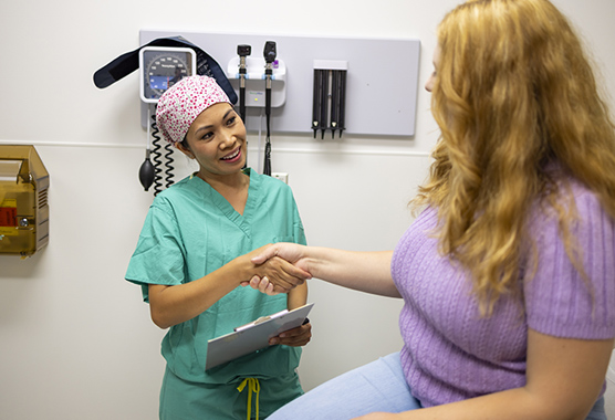 Female provider smiling and shaking hands with woman sitting on an exam table 