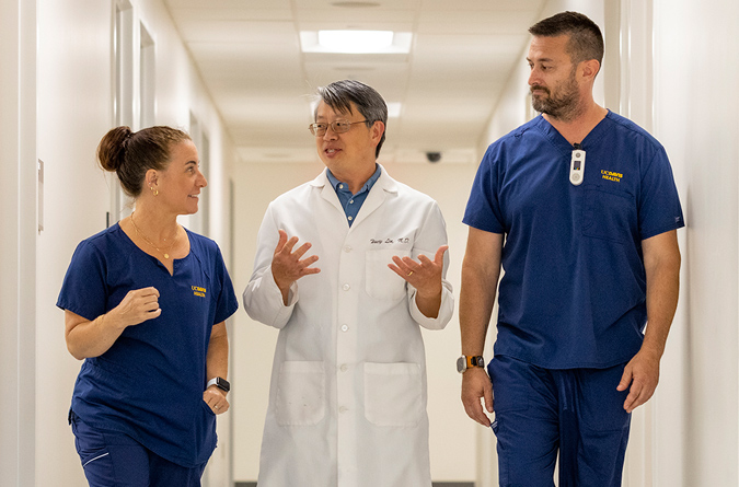 Three health care providers walking down a clinic hallway talking.