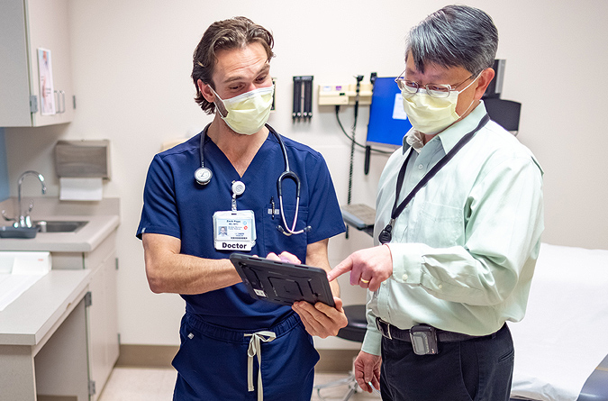 Two health care providers talking in an exam room while looking at a mobile tablet.