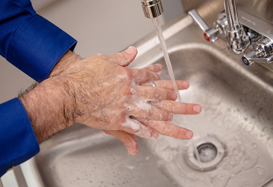 A man washing his hands in a stainless-steel sink.