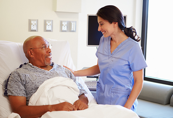 Man in hospital bed looking up and talking to female health care provider.