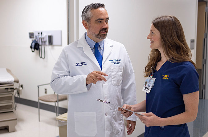 Physician talking with nurse who’s holding a clipboard outside a patient room.