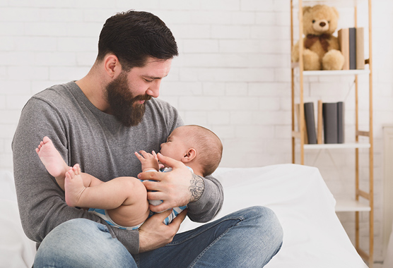 Father holding his crying baby while sitting on the edge of the bed.