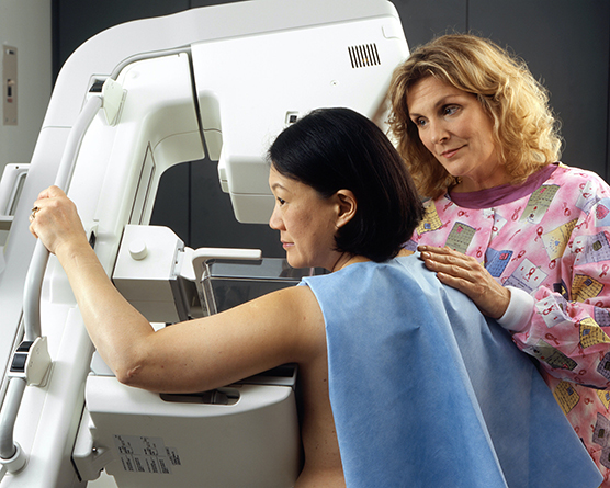 A female technician positioning a woman at an imaging machine to receive a mammogram.