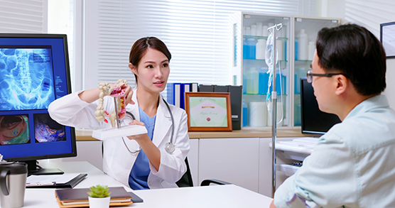 Female doctor wearing a white coat and stethoscope explaining colon model to a male patient.