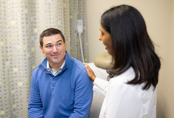 Male patient in an exam room smiling at a female physician who is touching his shoulder.