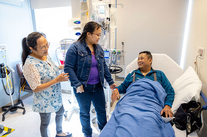 Cancer patient in a hospital bed laughing and holding hands with two famiy members