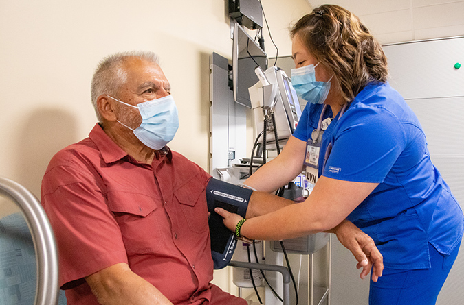 An older man getting his blood pressure checked by a nurse in blue scrubs.