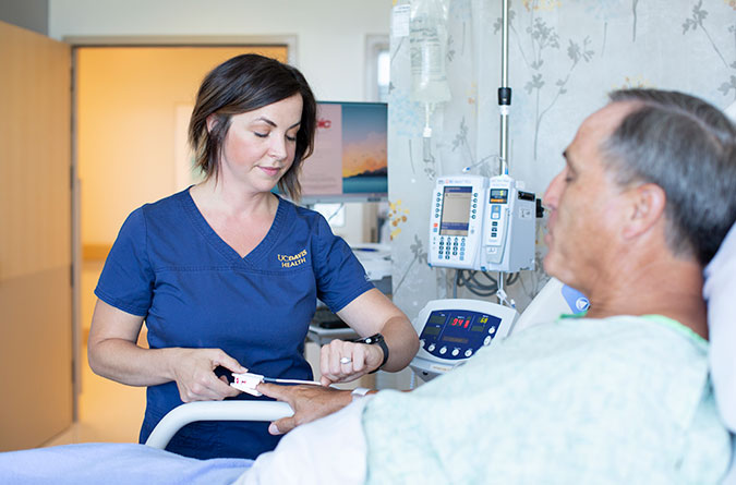 Female nurse checking the pulse of a male patient in a hospital bed