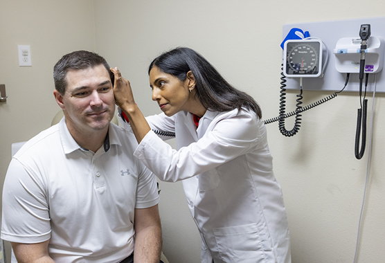 Female health care provider looking inside male patient’s ear at ear, nose and throat clinic 