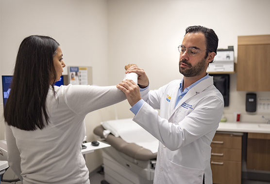 Sports medicine physician examining female patient’s elbow in a clinic.