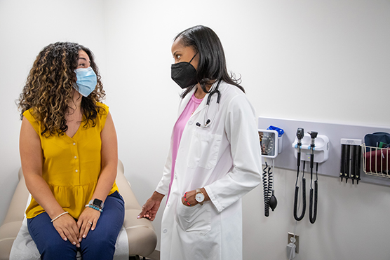 Female patient and female physician wearing masks in an exam room.