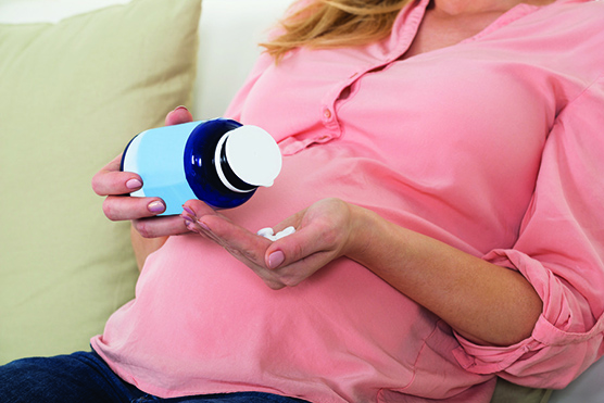Midsection of pregnant woman pouring pills in hand from bottle.