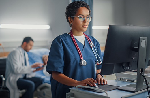 Health care professional documenting on computer as patient recovers from brain tumor surgery.