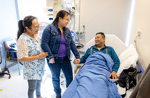 Patient in the hospital bed holding the hand of a loved one.