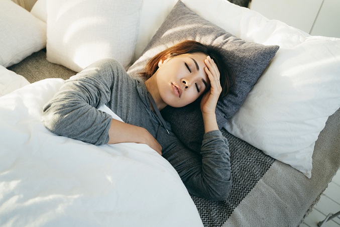 Woman laying in bed holding her head.