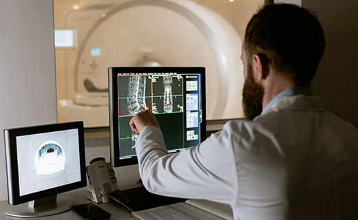 Doctor in white coat reviewing CT scans of a spine.