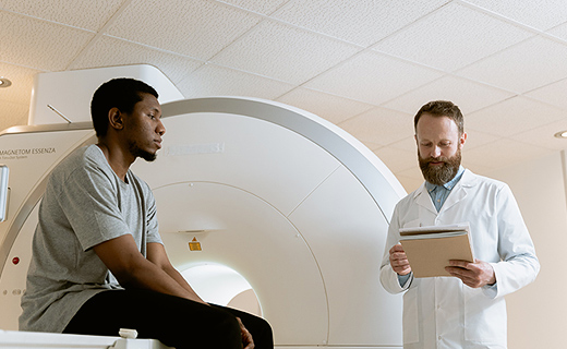 A patient sitting on CT machine bed speaking with a doctor.