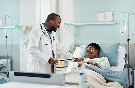 Woman laying in a hospital bed after epilepsy surgery with health care provider checking on her.