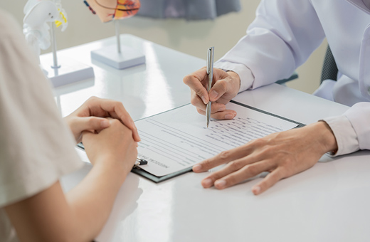 Healthcare worker explaining surgery to patient sitting at a table with a clipboard and paper.