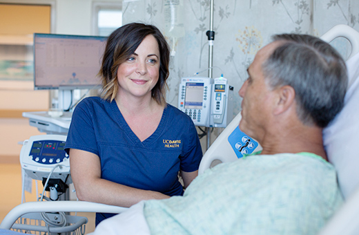 Female nurse taking care of older male patient laying in a hospital bed.