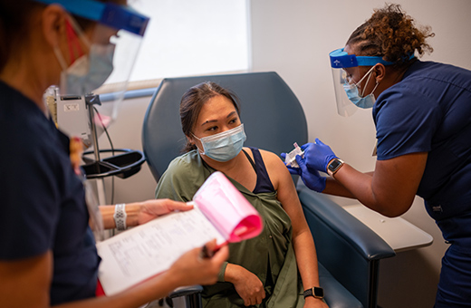 Female patient receiving an injection from one nurse while second nurse is looking through paperwork