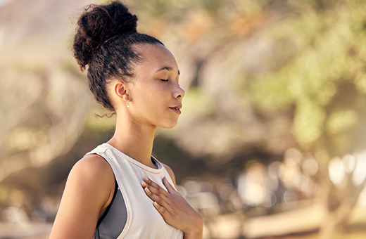 Woman taking a deep breath with her hand on her chest outside.