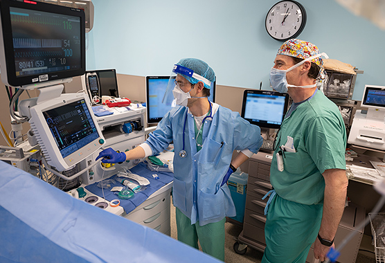 Two male anesthesiologists monitoring patient’s vital signs on screens during surgery.