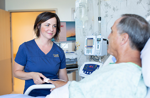 Male patient in a hospital bed looking at a female nurse who is smiling at the patient