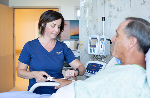 Health care provider checking vitals on male patient in hospital room after pain neurosurgery.