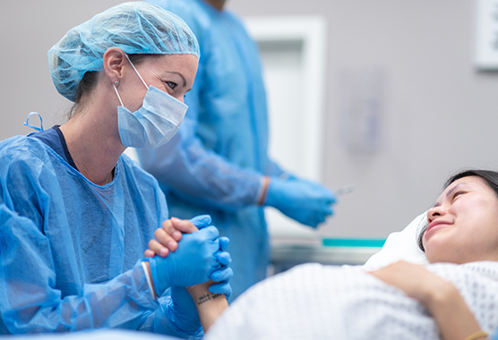 Pregnant woman looking at female health care provider while holding hands in delivery room.