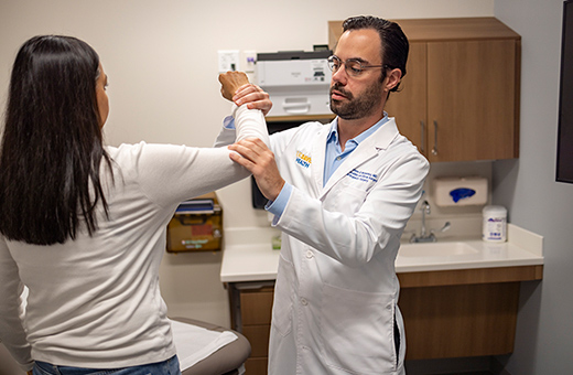 Orthopaedic surgeon examining a female patient’s arm in a clinic.