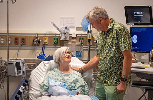 Female patient in a hospital bed preparing for knee replacement with a man smiling looking down next to her.