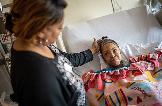 Daughter laying in hospital bed with mom looking on.