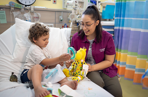 Child Life Specialist playing with child in hospital bed before pediatric neurosurgery.