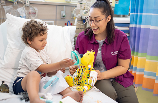 Young boy playing with a stuffed animal alongside a child life specialist.